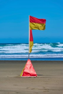 A red and yellow coastguard banner on the beach against a backdrop of waves under a clear blue sky,