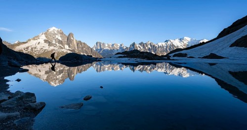 Mountaineer, silhouette in front of mountain landscape in the evening light, water reflection in