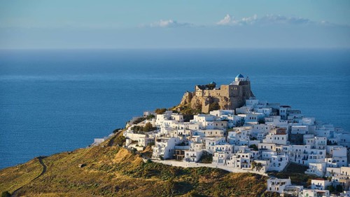 Panorama with white buildings on a hill, dense waves surrounding an old fortress by the sea,