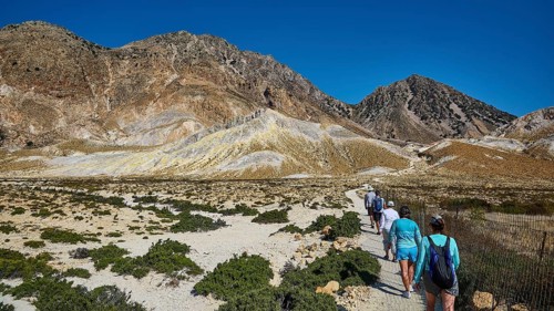 People walking on a path through a mountainous landscape under a clear sky, volcanism, volcanic