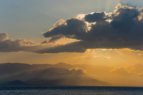 Dramatic sunset over the sea with clouds and mountains, radiant light and calm atmosphere, Agia