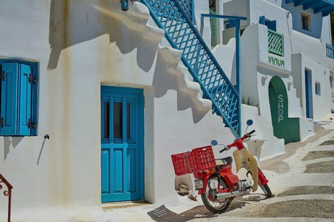 Entrance of a small shop in a Mediterranean setting with a red scooter and stairs, Chora,