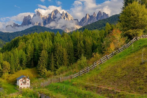 View of the partly cloudy Geisler group with a garden and a house in the foreground, Dolomites,