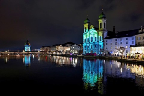 Water tower and Jesuit church on the right with light installation, on the Reuss at dusk, Old Town,
