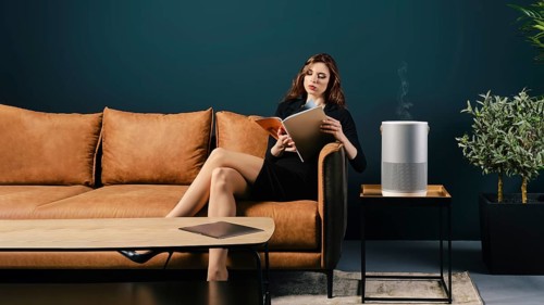Young well dressed woman sits on couch in lobby near air purifier and reading magazine