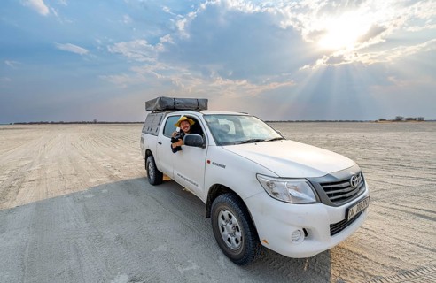 Young man with camera looking out the window of an off-road vehicle, Toyota Hilux on a salt pan,