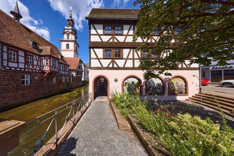 River Mümling, half-timbered houses, archway, church tower, metal railing, flower bed, blue sky