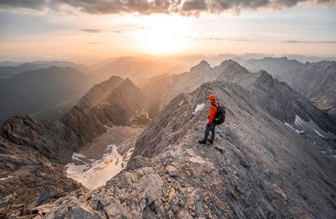Mountaineer with helmet on a narrow rocky ridge at sunrise, crossing the Jubiläumsgrat, view of