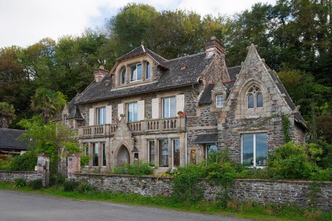 Historic stone house surrounded by trees with elaborate details and large windows,