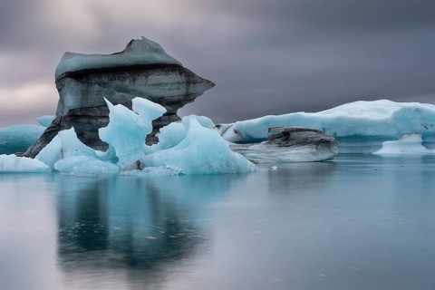 Iceberg formations are reflected in the still water under an overcast sky, Jökulsárlón glacier