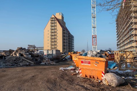 Construction site with high-rise building and crane, surrounded by piles of rubble, old warehouse