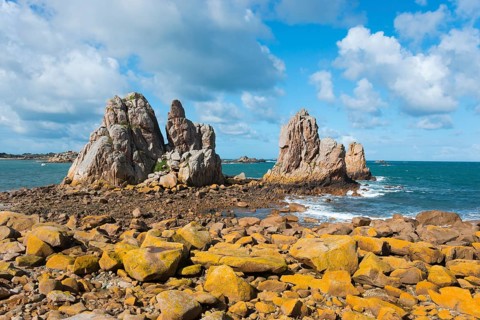 Rocky coast with stormy waves under a blue sky with white clouds, Plage de Pors Scaff,