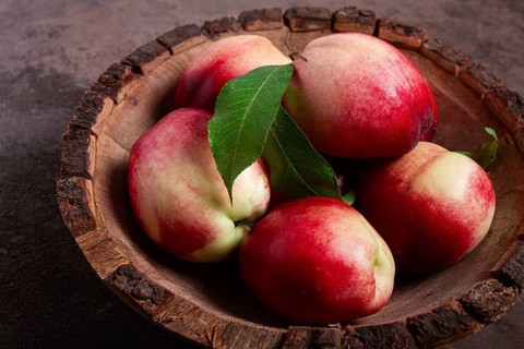 Ripe nectarine, in a wooden plate, brown background, top view, no people