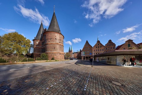 Lübeck Holstentor, side view, pedestrian crossing, cobblestone pavement, blue sky with fair weather