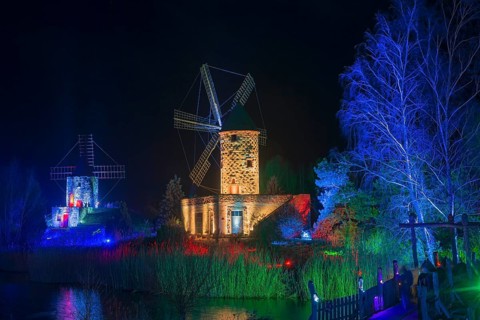 Two windmills in a nocturnal scene, illuminated with colourful lights and surrounded by water,