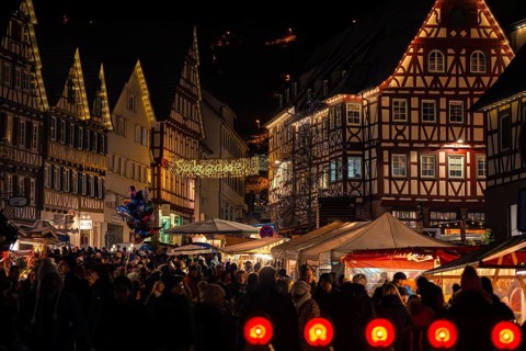 Densely packed crowd at an atmospherically illuminated Christmas market with half-timbered houses,