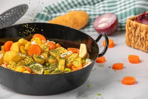 Parsley falls onto chopped vegetables and potatoes in a saucepan, surrounded by fresh ingredients
