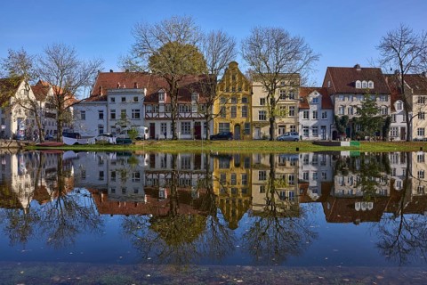 Historic houses, symmetrical reflections on the water surface, river Trave, cloudless blue sky, old