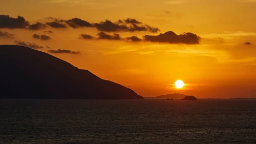 Still life of a sunset over the sea with mountains on the horizon and a sky in yellow and orange,