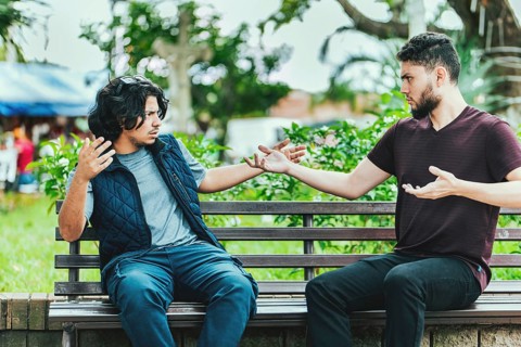 Two people arguing on a park bench. Two guys arguing sitting on a bench