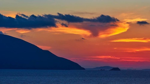 Play of colours in the evening sky over the sea, hills as silhouettes in front of a colourful