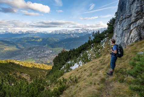 Mountaineer on a narrow hiking trail between mountain pines, view of Garmisch-Partenkirchen and