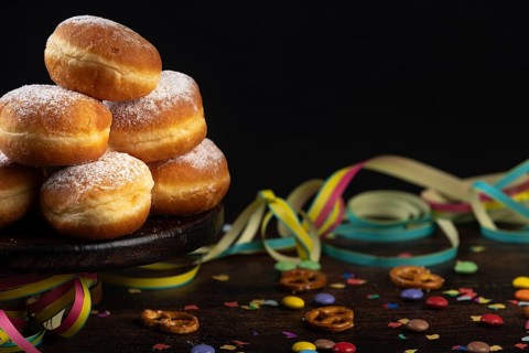 Berliners, doughnuts with icing sugar are piled up against a dark background next to confetti and