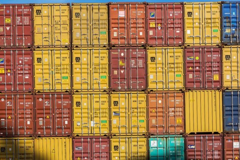 Rows of stacked yellow, reddish brown, blue, orange and turquoise metal box shipping containers on