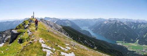 Mountaineer on the summit ridge of Hochunnütz with summit cross, behind Achensee and summit of