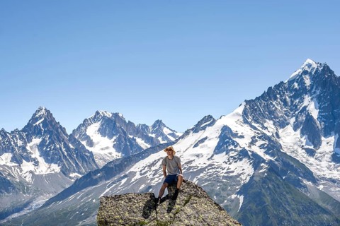 Mountaineer sitting on a rock and looking into the camera, mountain landscape with mountain peak