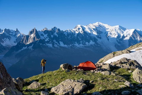 Photographer with telephoto lens next to red tent, mountain landscape in the morning light,
