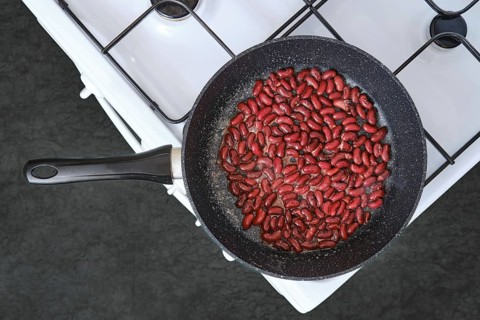 Red kidney beans are being cooked in a skillet placed on a gas stove in a home kitchen setting. The