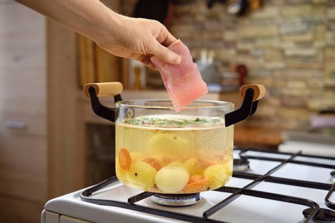 A hand gently places a piece of fish into a pot of simmering vegetable soup, enhancing the flavors.