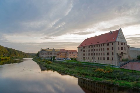 River landscape with buildings along the bank at dusk and reflection in the water, River Mulde,