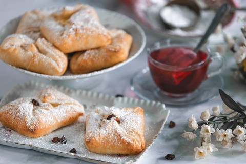 Delicious puff pastries, curd cheese golaches with icing sugar next to a cup of tea and decorative