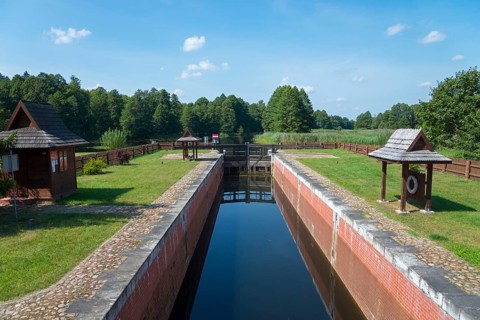 A narrow canal with a lock leads through a green forest landscape, Tartak Lock, Augustow Canal,