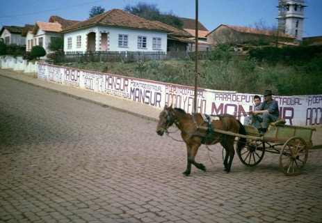 Man and boy riding on a horse-drawn cart past election campaign posters of politician João Mansur
