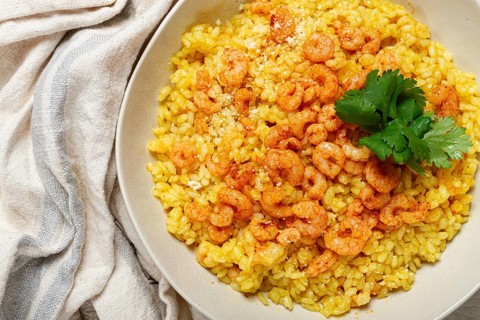 Risotto with shrimp, in a bowl, on a textured surface, with a side dish of fresh coriander,