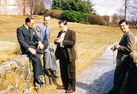 Four elegantly dressed men in business suits outdoors, USA around 1953, standing, sitting against