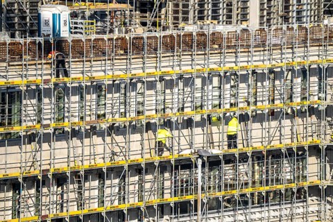 Large construction site, scaffolded new building, factory and office building, workers on the