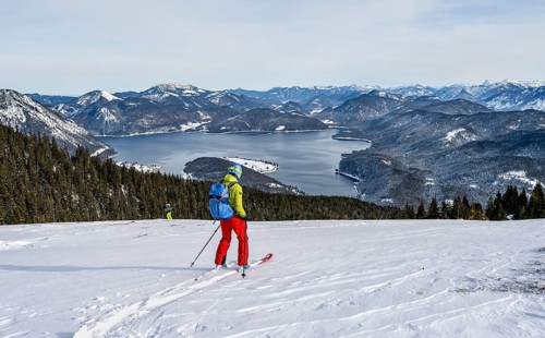 Skiers skiing down the Simetsberg, view of Walchensee and mountain panorama, Estergebirge, Bavarian