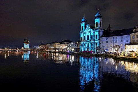 Water tower and Jesuit church on the right with light installation, on the Reuss at dusk, Old Town,
