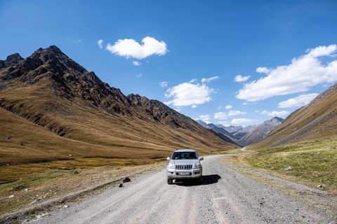 Off-road vehicle driving on a gravel track in a valley, picturesque mountain landscape with white