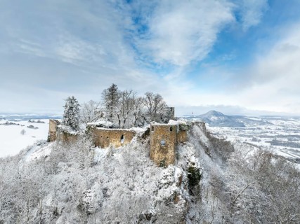 Aerial view of the snow-covered Hegau volcano Mägdeberg with remains of a castle wall on a cold