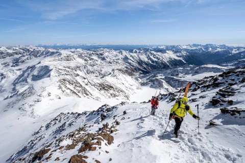 Ski tourers on foot, carrying skis on a rucksack, mountain panorama, snow-covered mountain