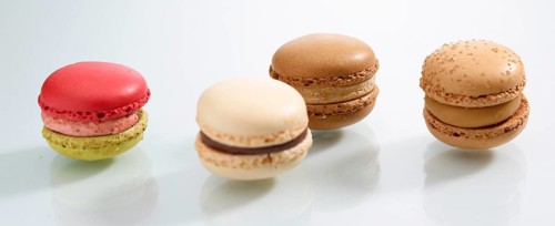 Four differently coloured macarons in front of a white background, studio shot