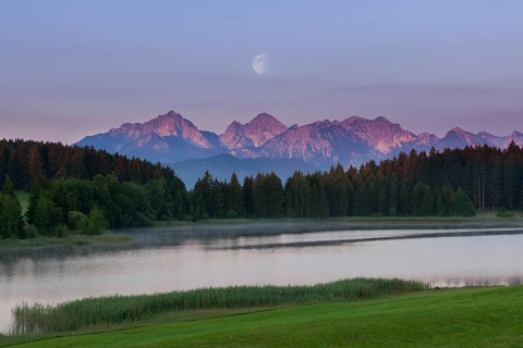Idyllic lake with mountain landscape at dawn, pink sky and moon, Hegratsrieder See near Füssen,