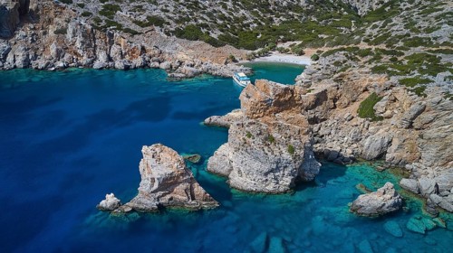 Palatia Beach, Palatia, rocks protrude from the turquoise blue sea near a boat on the rocky coast,