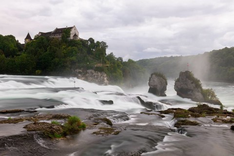 Dramatic waterfall flows past rocks to a castle, Schloss Laufen, Rhine Falls, Canton Schaffhausen,