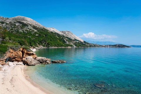 Clear blue sea water on a sandy beach with rocky coastline under a cloudless sky, bay near Stara